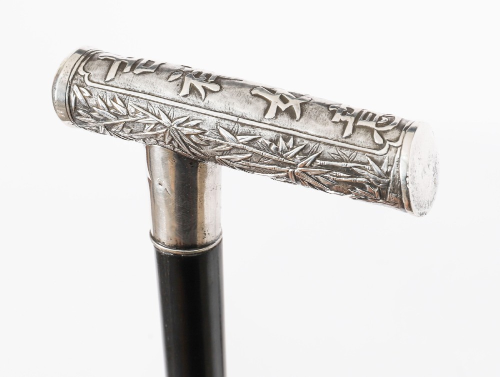 An antique walking stick featuring a relief-carved silver handle decorated with prunus blossoms, set on a slender black ebonised wooden shaft with a brass tip. View II