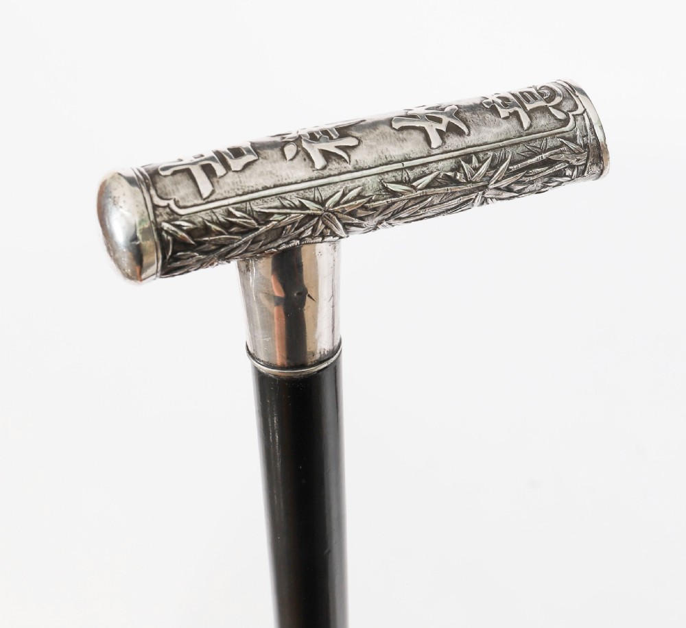 An antique walking stick featuring a relief-carved silver handle decorated with prunus blossoms, set on a slender black ebonised wooden shaft with a brass tip. View III