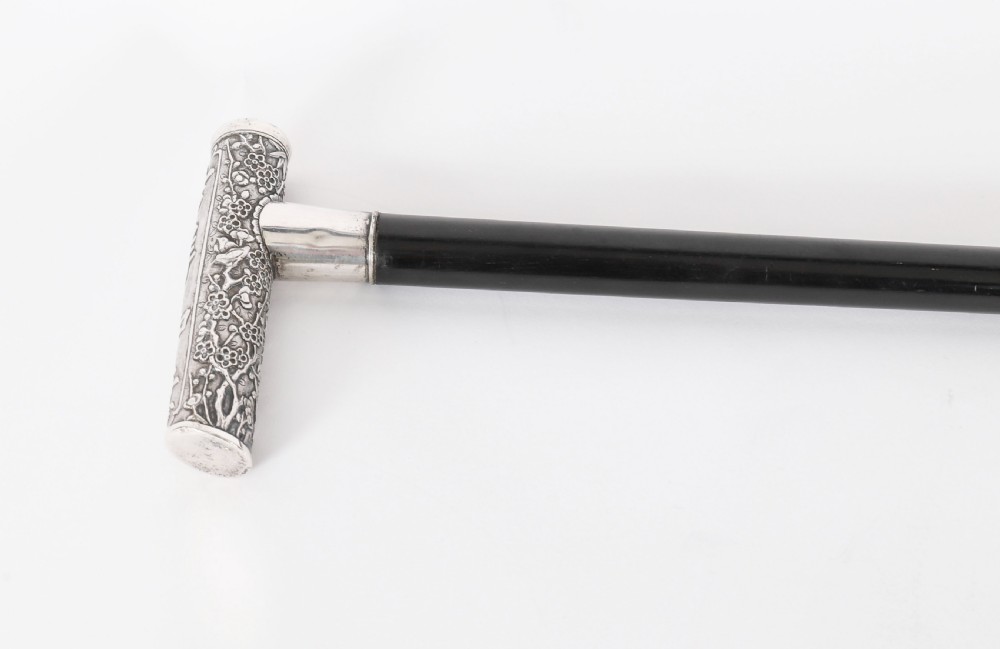 An antique walking stick featuring a relief-carved silver handle decorated with prunus blossoms, set on a slender black ebonised wooden shaft with a brass tip. View IV