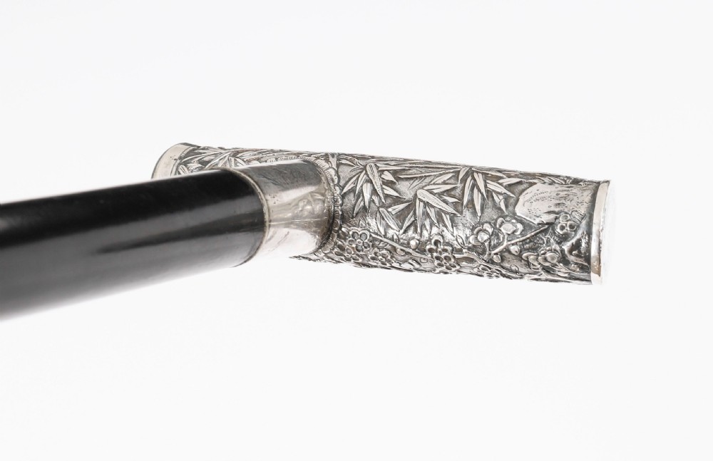 An antique walking stick featuring a relief-carved silver handle decorated with prunus blossoms, set on a slender black ebonised wooden shaft with a brass tip. View VI