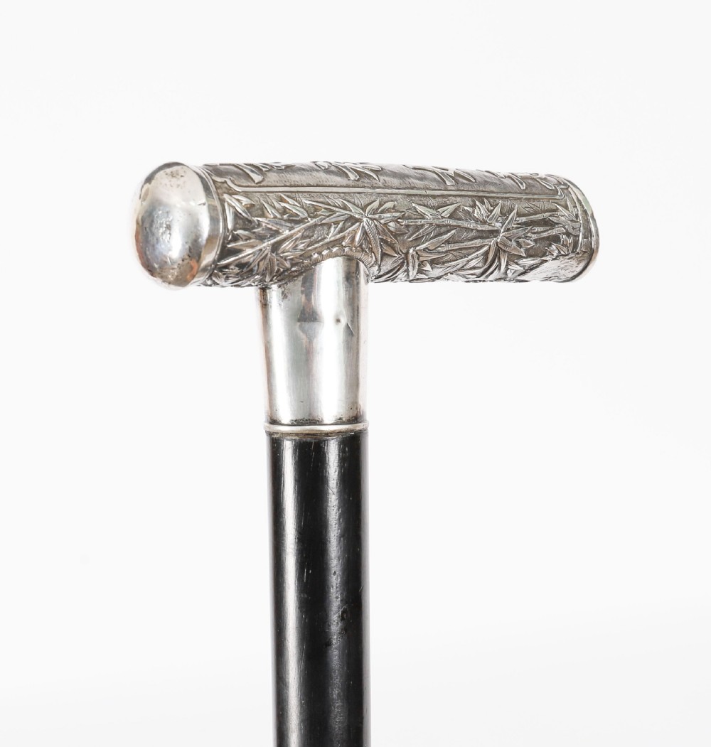 An antique walking stick featuring a relief-carved silver handle decorated with prunus blossoms, set on a slender black ebonised wooden shaft with a brass tip. View VII