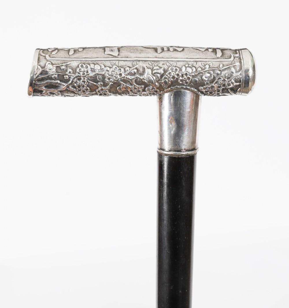 An antique walking stick featuring a relief-carved silver handle decorated with prunus blossoms, set on a slender black ebonised wooden shaft with a brass tip. View IX
