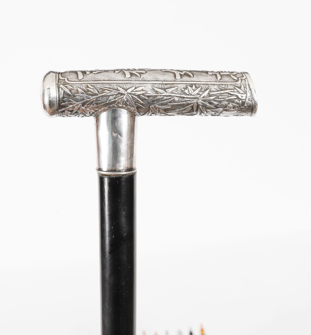 An antique walking stick featuring a relief-carved silver handle decorated with prunus blossoms, set on a slender black ebonised wooden shaft with a brass tip. View X