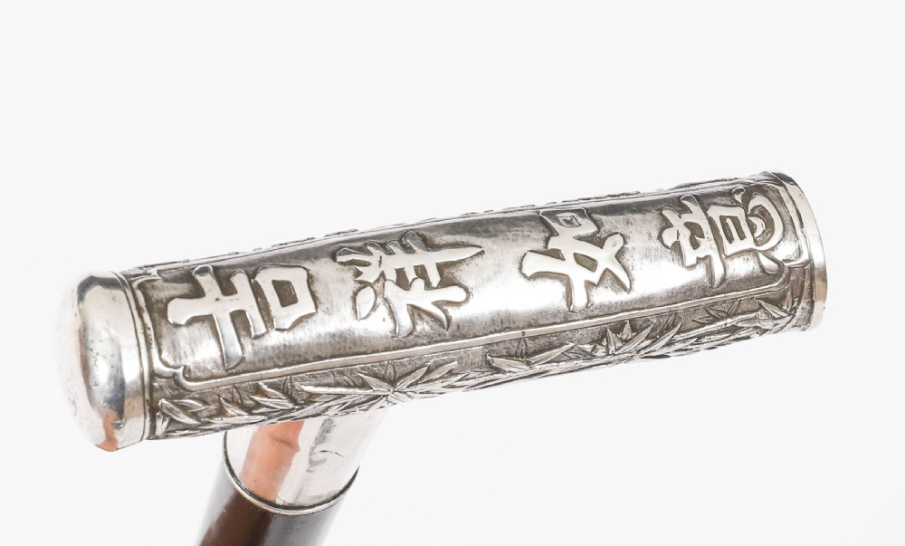 An antique walking stick featuring a relief-carved silver handle decorated with prunus blossoms, set on a slender black ebonised wooden shaft with a brass tip. View XII