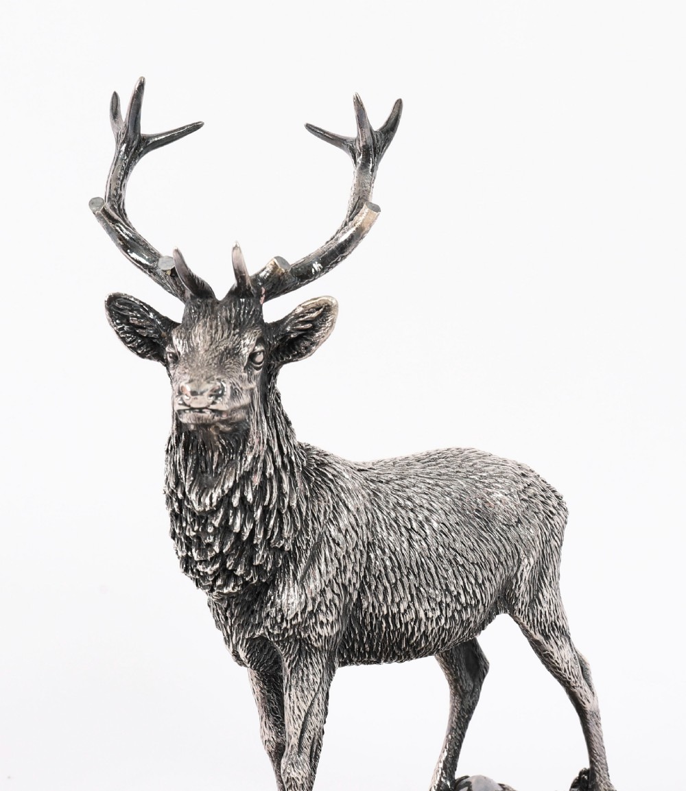 A detailed sterling silver sculpture of a standing stag with branching antlers positioned on a textured rocky ground base. View III