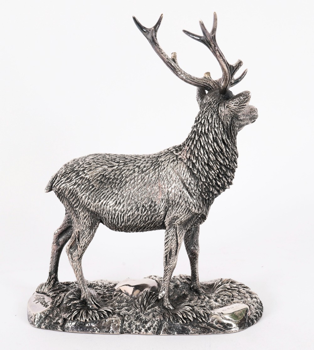 A detailed sterling silver sculpture of a standing stag with branching antlers positioned on a textured rocky ground base. View IV