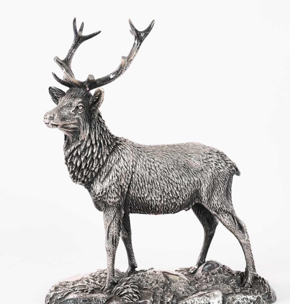 A detailed sterling silver sculpture of a standing stag with branching antlers positioned on a textured rocky ground base. View V