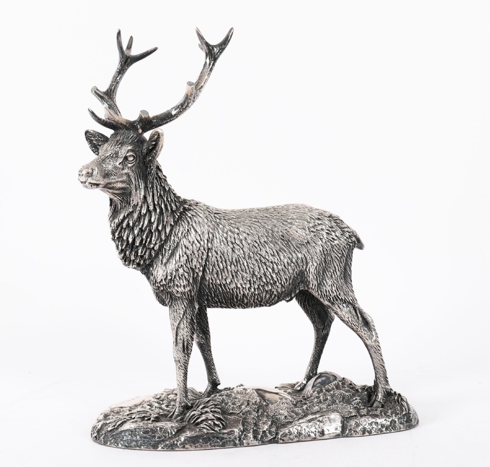A detailed sterling silver sculpture of a standing stag with branching antlers positioned on a textured rocky ground base. View VI