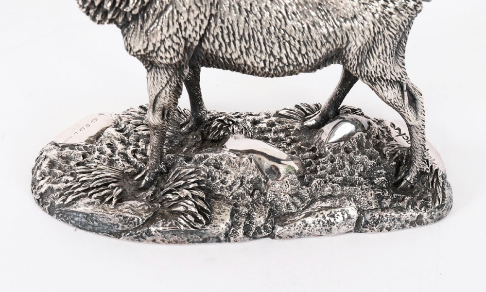 A detailed sterling silver sculpture of a standing stag with branching antlers positioned on a textured rocky ground base. View XII