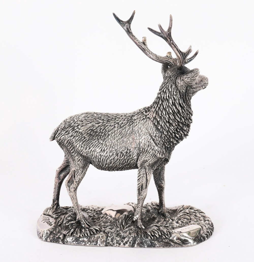 A detailed sterling silver sculpture of a standing stag with branching antlers positioned on a textured rocky ground base. View XIII