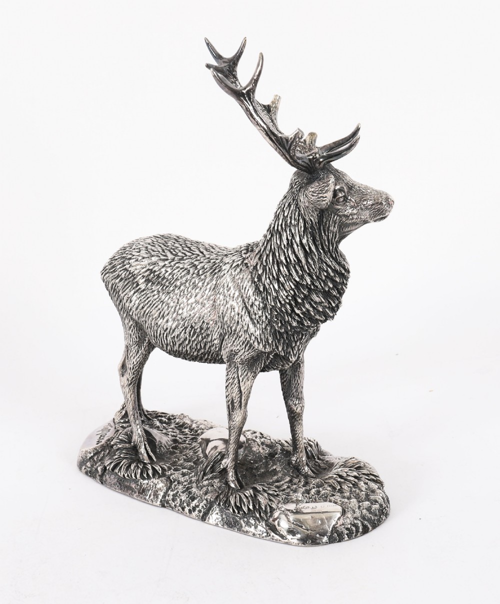 A detailed sterling silver sculpture of a standing stag with branching antlers positioned on a textured rocky ground base. View XIV