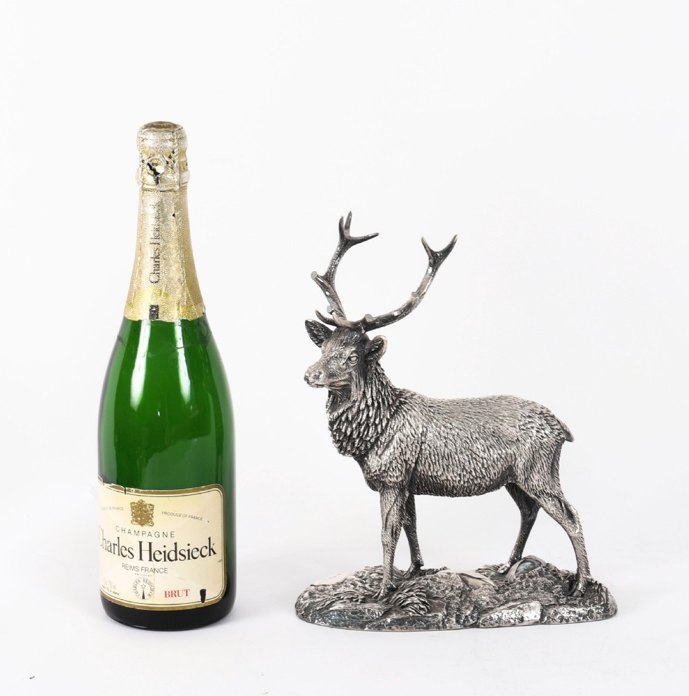 A detailed sterling silver sculpture of a standing stag with branching antlers positioned on a textured rocky ground base. View XV