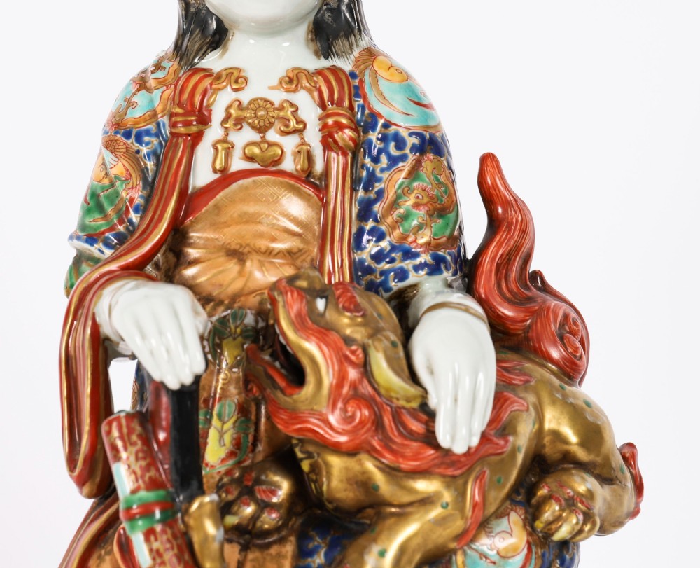 An antique Japanese Kutani porcelain sculpture depicting Guanyin standing beside a shishi lion with detailed polychrome drapery and gold leaf accents. View V