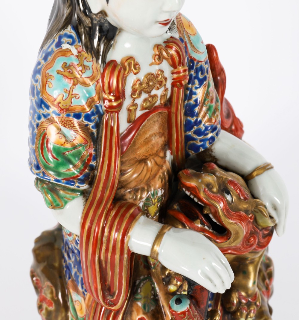 An antique Japanese Kutani porcelain sculpture depicting Guanyin standing beside a shishi lion with detailed polychrome drapery and gold leaf accents. View IX