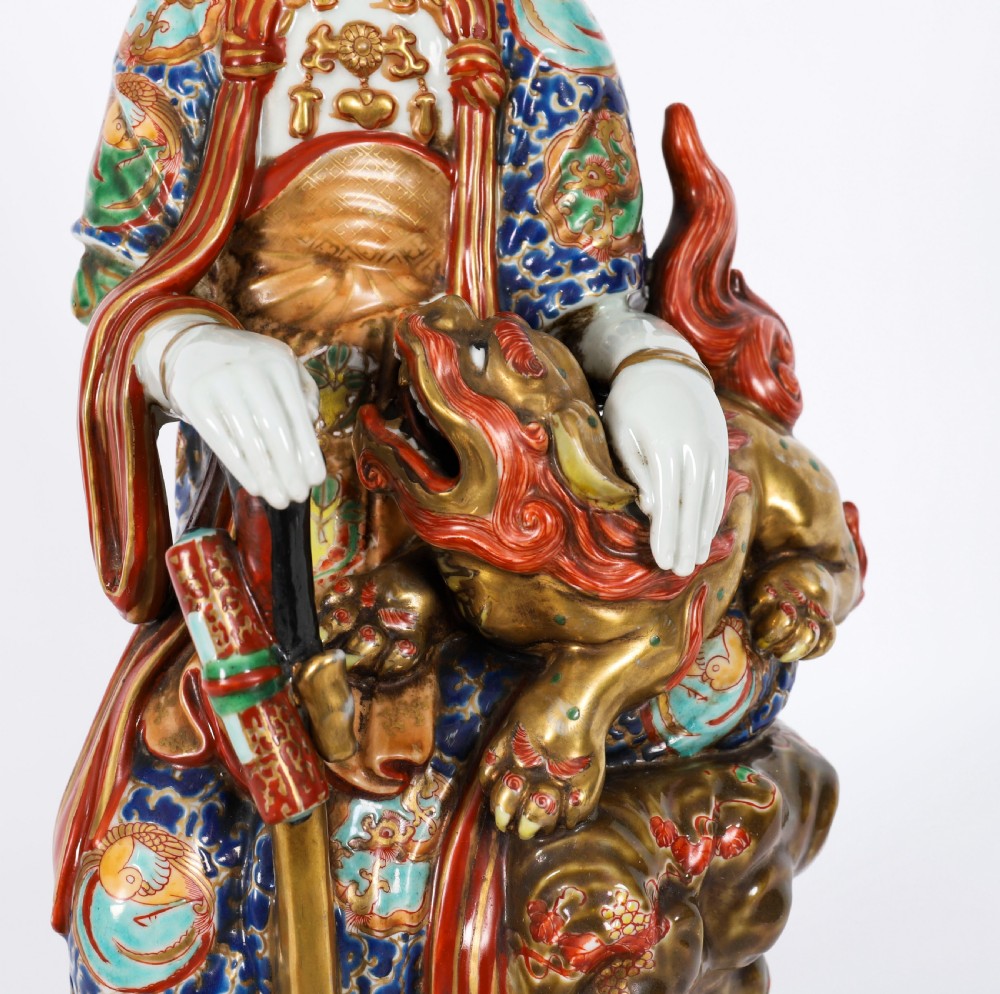 An antique Japanese Kutani porcelain sculpture depicting Guanyin standing beside a shishi lion with detailed polychrome drapery and gold leaf accents. View XIV