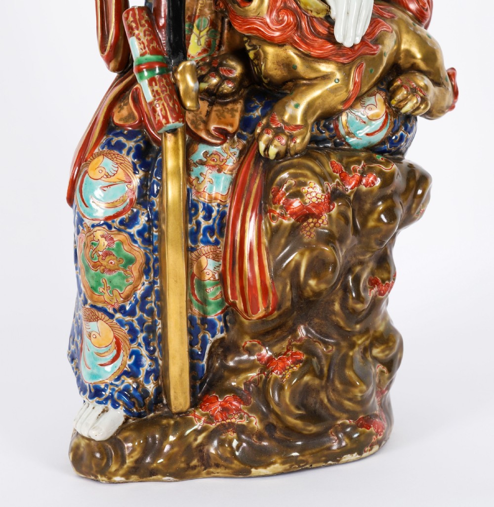 An antique Japanese Kutani porcelain sculpture depicting Guanyin standing beside a shishi lion with detailed polychrome drapery and gold leaf accents. View XVIII