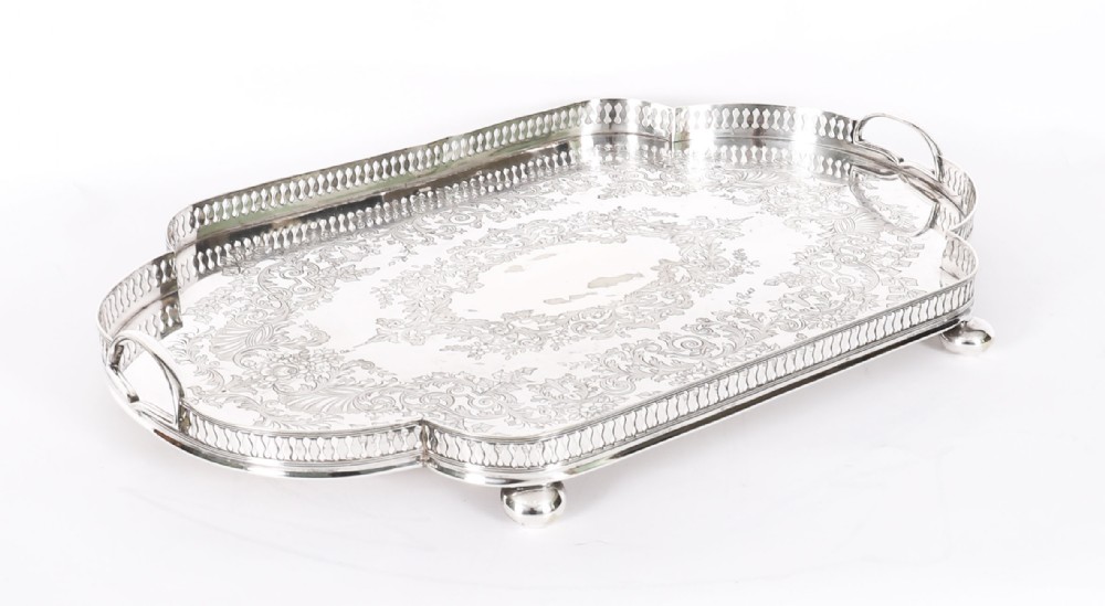 An Edwardian silver-plated gallery tray featuring a pierced rim, engraved foliate scrollwork, twin handles, and ball feet.