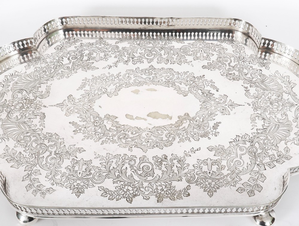 An Edwardian silver-plated gallery tray featuring a pierced rim, engraved foliate scrollwork, twin handles, and ball feet. View III