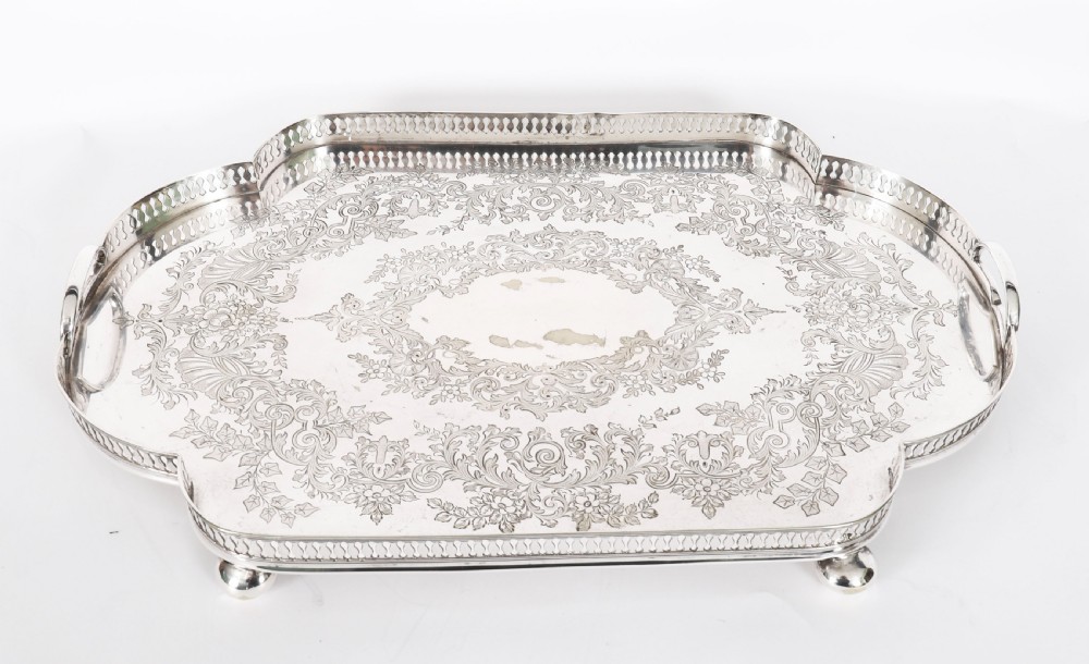 An Edwardian silver-plated gallery tray featuring a pierced rim, engraved foliate scrollwork, twin handles, and ball feet. View VIII