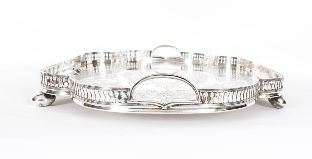 An Edwardian silver-plated gallery tray featuring a pierced rim, engraved foliate scrollwork, twin handles, and ball feet. View X