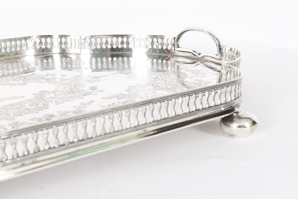 An Edwardian silver-plated gallery tray featuring a pierced rim, engraved foliate scrollwork, twin handles, and ball feet. View XI