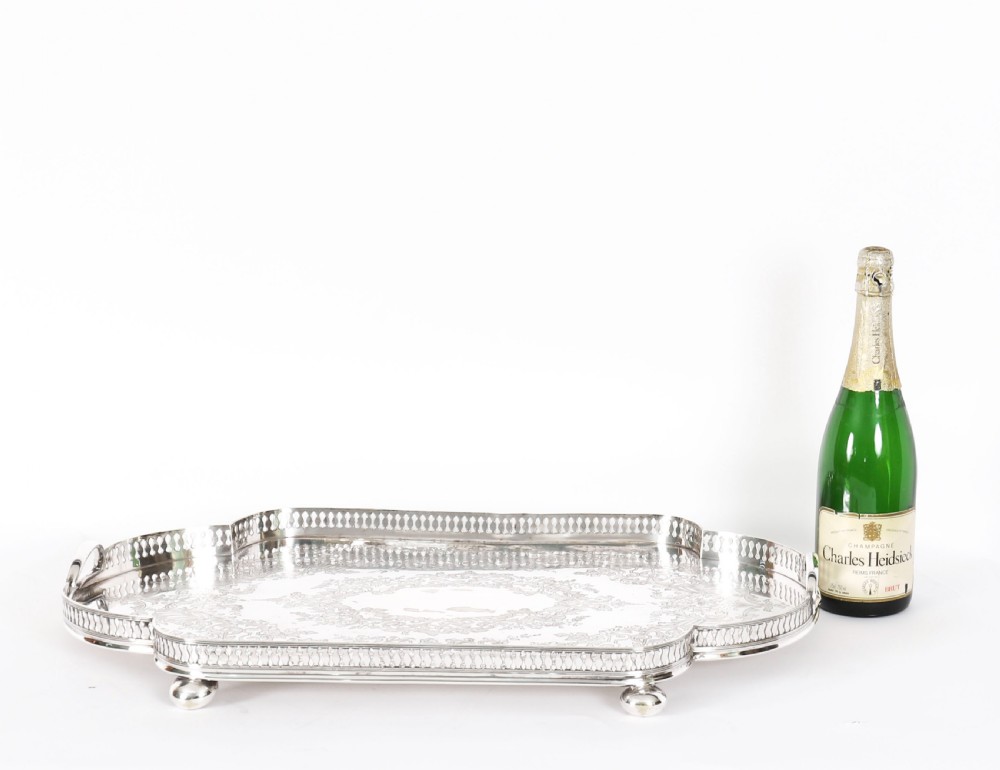 An Edwardian silver-plated gallery tray featuring a pierced rim, engraved foliate scrollwork, twin handles, and ball feet. View XV