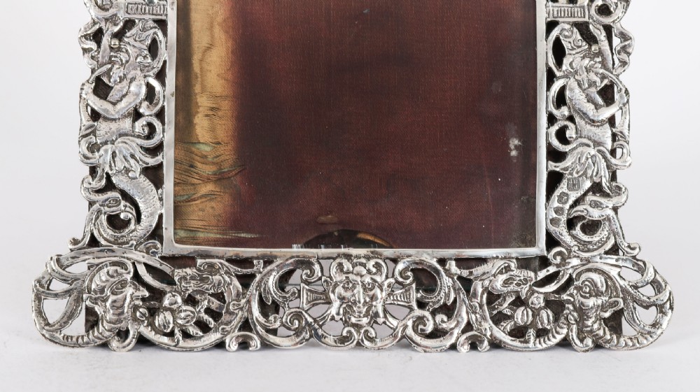 An antique sterling silver photo frame featuring openwork scrollwork detailing and a dark wooden easel back. View IV