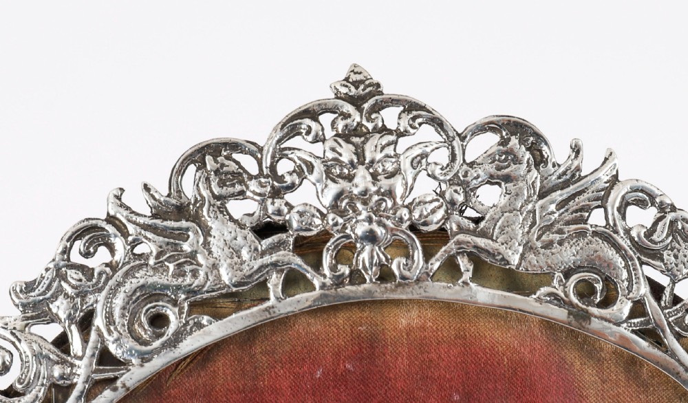 An antique sterling silver photo frame featuring openwork scrollwork detailing and a dark wooden easel back. View VII
