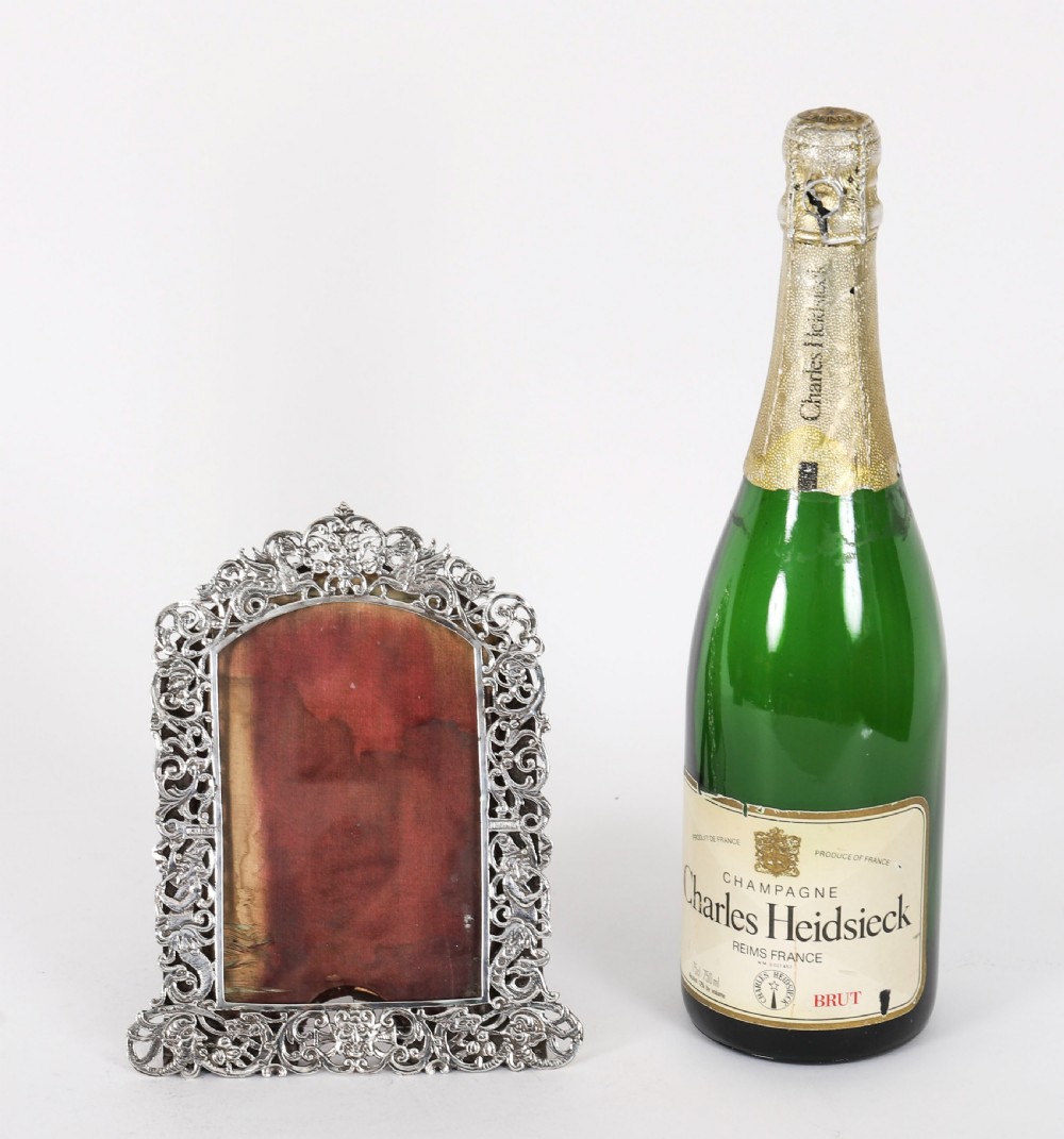An antique sterling silver photo frame featuring openwork scrollwork detailing and a dark wooden easel back. View XIV