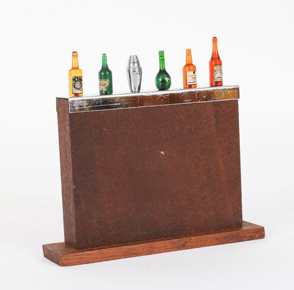 An Art Deco wooden cocktail stick holder featuring miniature liquor bottle handles and a central cocktail shaker pick atop a chrome-trimmed base. View VII