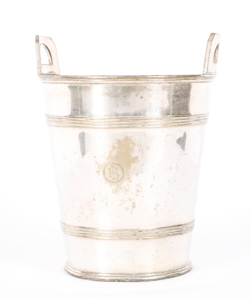 An Art Deco silver-plated champagne cooler featuring angular raised handles, horizontal reeded bands, and an engraved circular crest.