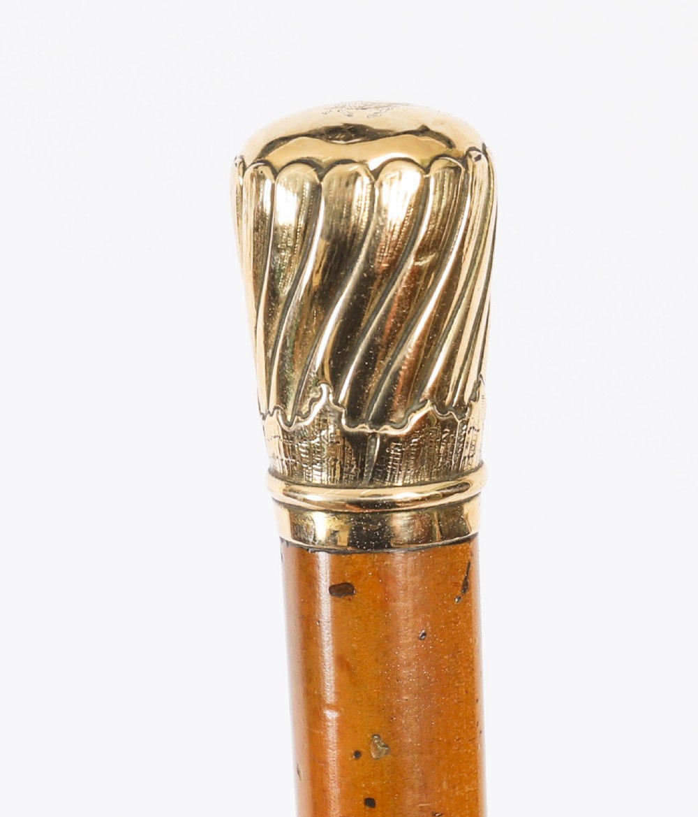 A straight polished wooden walking cane featuring a decorated 18ct gold pommel handle and a metal ferrule tip at the base. View X