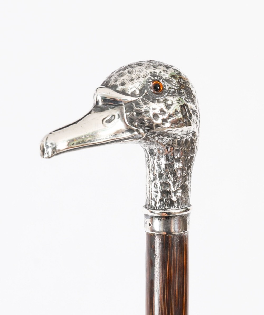 An antique walking stick featuring a dark polished wooden shaft topped with a cast silver duck head handle. View IX