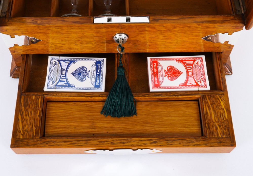 An antique blonde oak tantalus featuring three square cut-glass decanters set against a mirror back, decorative silver-plated corner mounts, and a lower drawer with a key. View IX