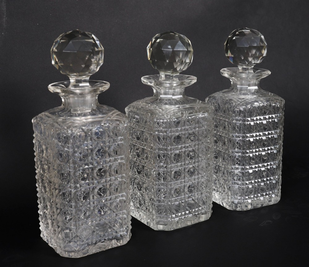 An antique blonde oak tantalus featuring three square cut-glass decanters set against a mirror back, decorative silver-plated corner mounts, and a lower drawer with a key. View XII