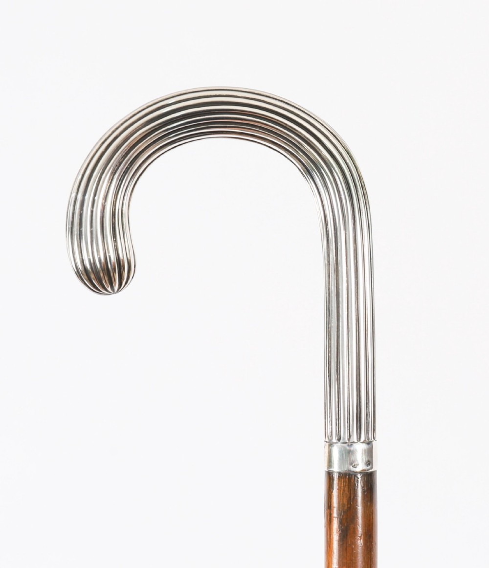 An antique walking stick featuring a fluted silver crook handle mounted on a dark polished wooden shaft.