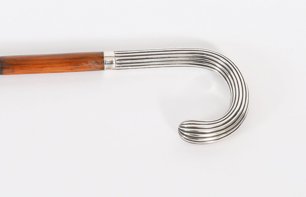 An antique walking stick featuring a fluted silver crook handle mounted on a dark polished wooden shaft. View IV