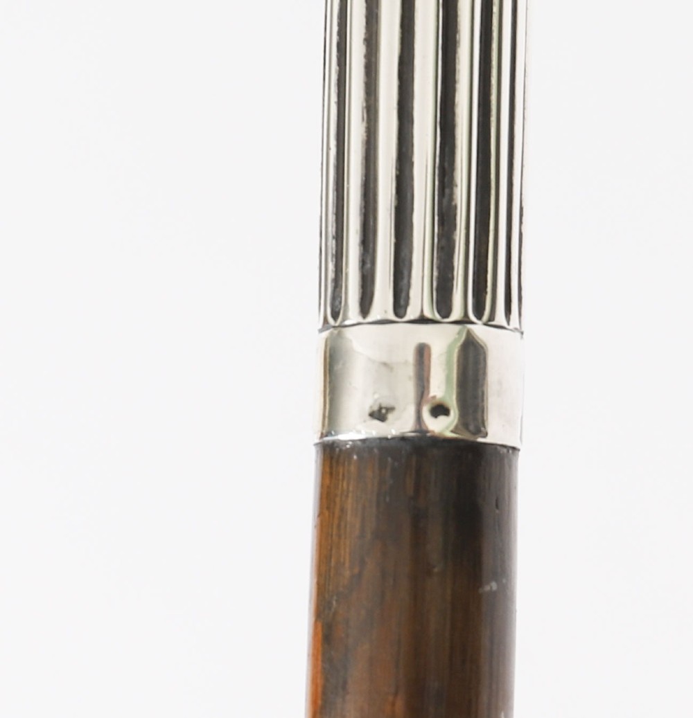 An antique walking stick featuring a fluted silver crook handle mounted on a dark polished wooden shaft. View VI