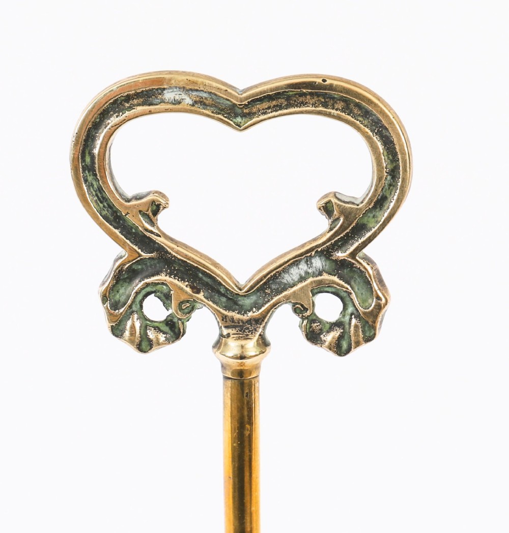 A 19th-century Victorian brass door stop featuring a tall shaft topped with a heart-shaped handle and supported by a heavy, tiered circular base. View V
