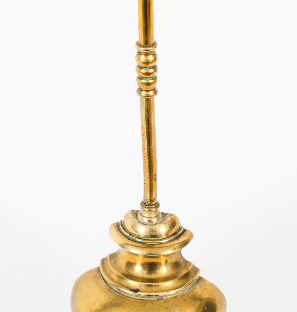 A 19th-century Victorian brass door stop featuring a tall shaft topped with a heart-shaped handle and supported by a heavy, tiered circular base. View VI