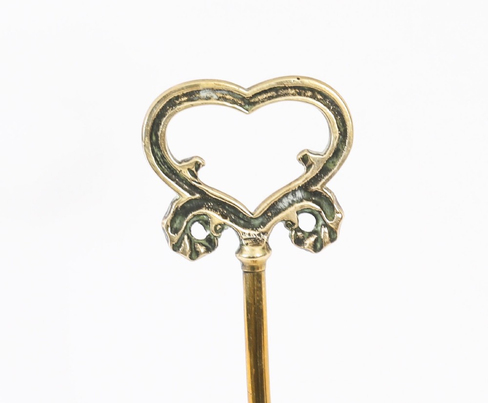 A 19th-century Victorian brass door stop featuring a tall shaft topped with a heart-shaped handle and supported by a heavy, tiered circular base. View XI