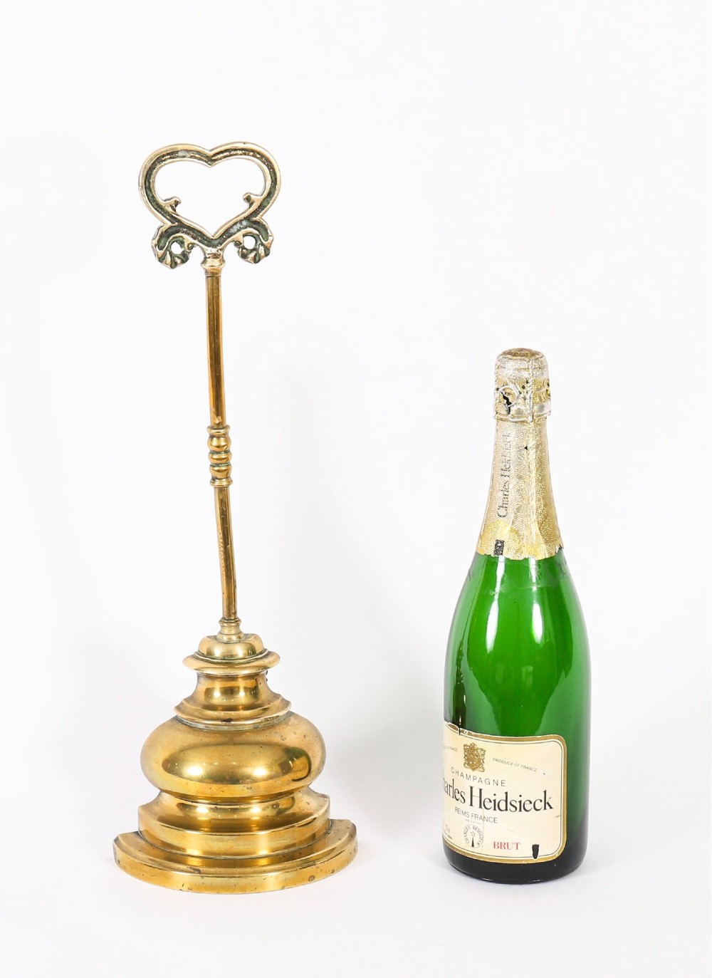 A 19th-century Victorian brass door stop featuring a tall shaft topped with a heart-shaped handle and supported by a heavy, tiered circular base. View XIII