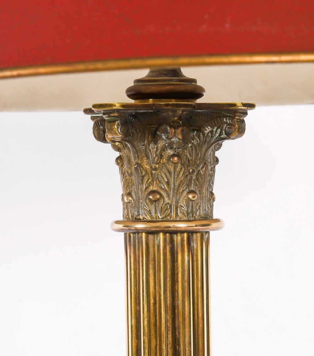 A pair of late nineteenth-century brass Corinthian column table lamps featuring fluted stems, stepped bases, wooden plinths, and conical red lampshades. View XII