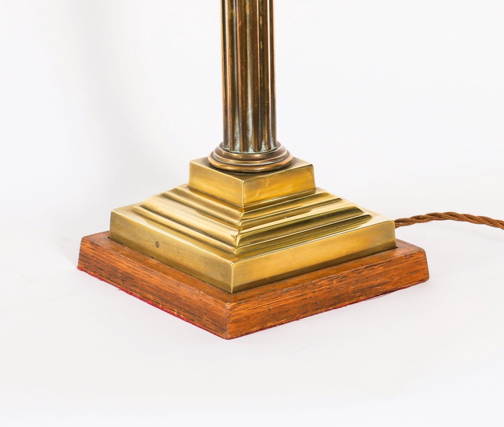 A pair of late nineteenth-century brass Corinthian column table lamps featuring fluted stems, stepped bases, wooden plinths, and conical red lampshades. View XV