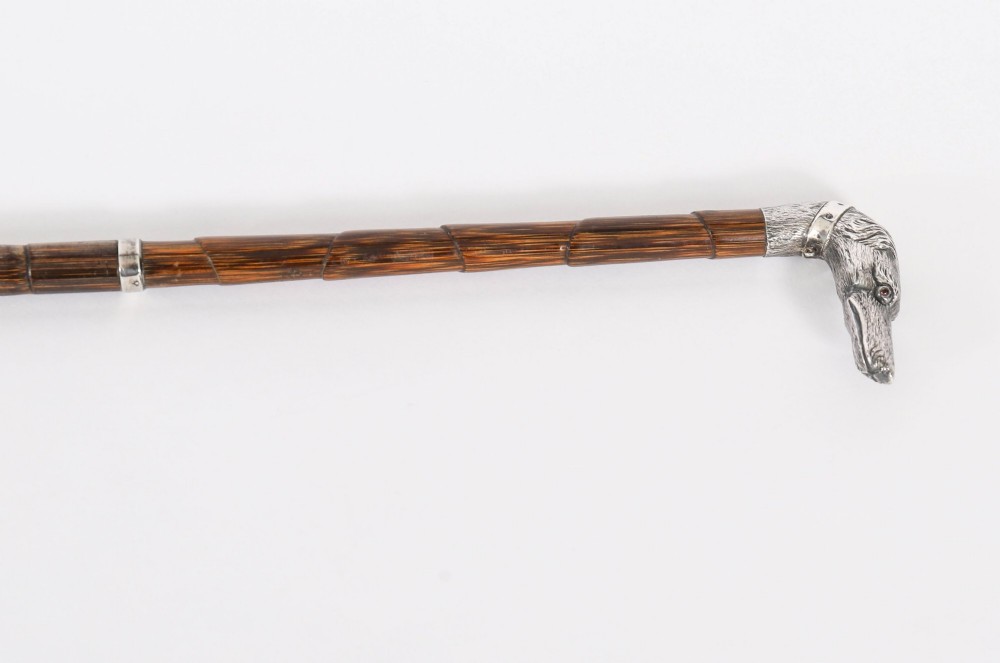 An antique walking stick featuring a sculpted silver greyhound head handle with hallmarks set upon a dark polished wood shaft. View IV