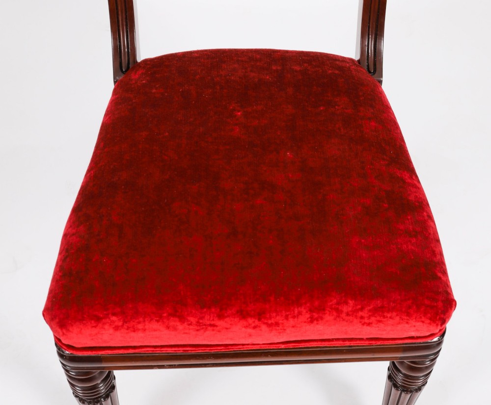 A set of ten Regency flame mahogany dining chairs with carved scroll backrails, turned fluted front legs, and red velvet seats. View XI