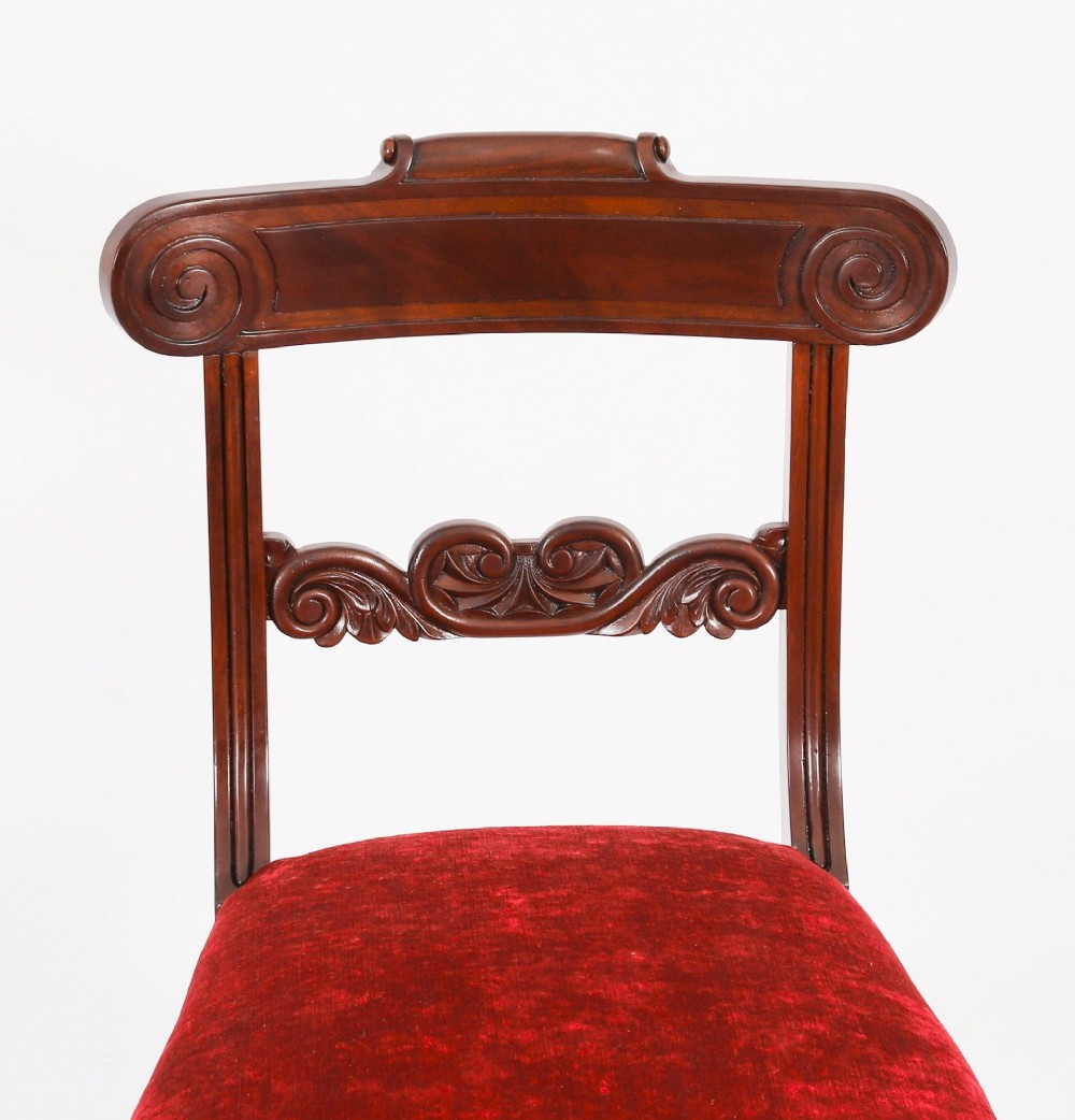 A set of ten Regency flame mahogany dining chairs with carved scroll backrails, turned fluted front legs, and red velvet seats. View XII