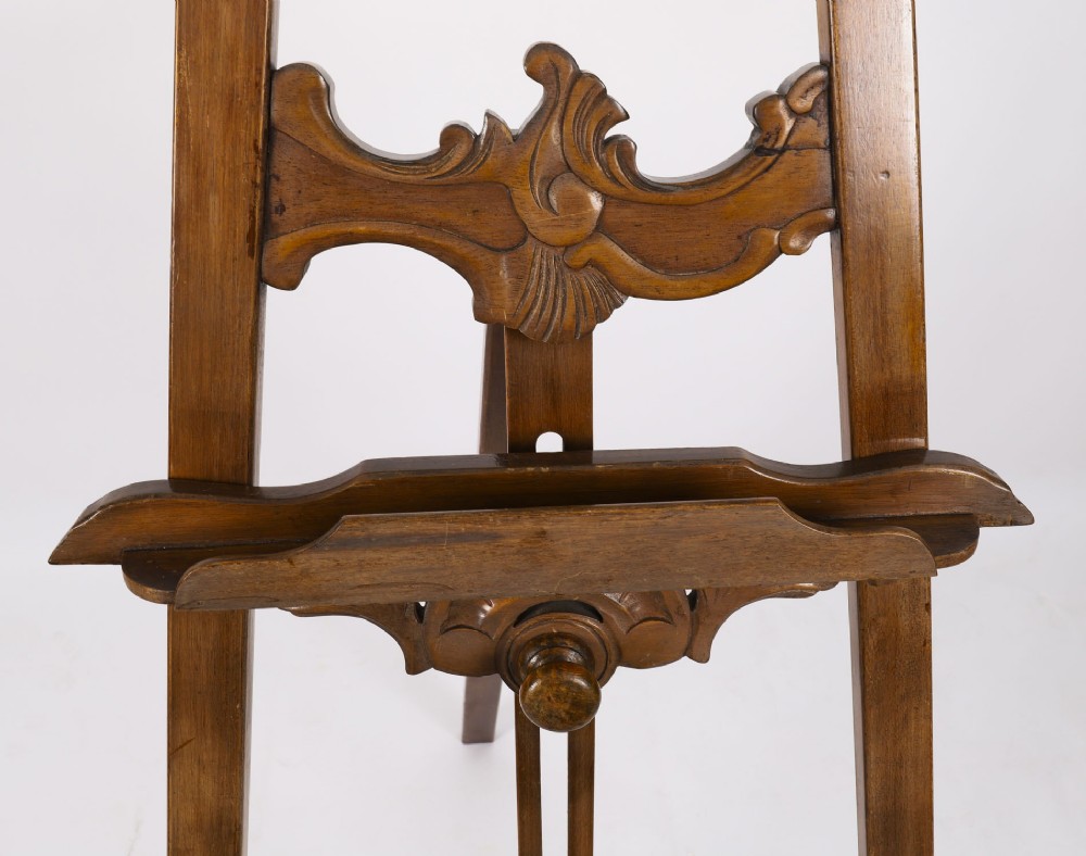 A 19th-century carved walnut artist easel featuring an ornate Rococo Revival scrollwork crest and an adjustable ledge on a tripod frame. View VII