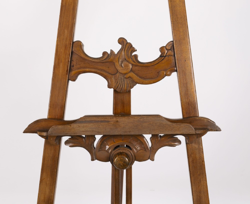 A 19th-century carved walnut artist easel featuring an ornate Rococo Revival scrollwork crest and an adjustable ledge on a tripod frame. View VIII