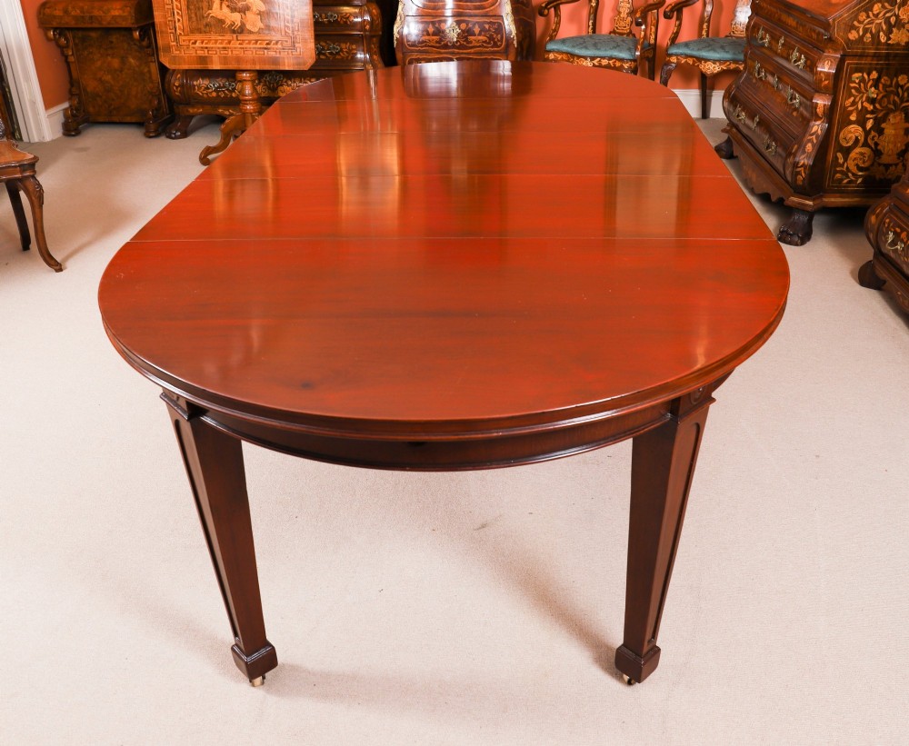 An antique Victorian oval extending dining table crafted from flame mahogany with tapered legs on brass castors. View II